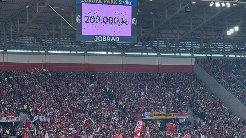 Der Screen im Europa-Park Stadion zeigt an, dass die 200.000 Fahrrad-Fan-Zahl erreicht wurde. Davor sieht man Spieler auf dem Spielfeld. Der Screen im Europa-Park Stadion zeigt an, dass die 200.000 Fahrrad-Fan-Zahl erreicht wurde. Davor sieht man Spieler auf dem Spielfeld.