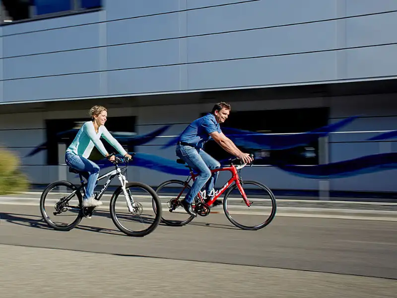 Zwei Menschen, die auf zwei Stadträdern vor einem Büro-Gebäude vorbeifahren